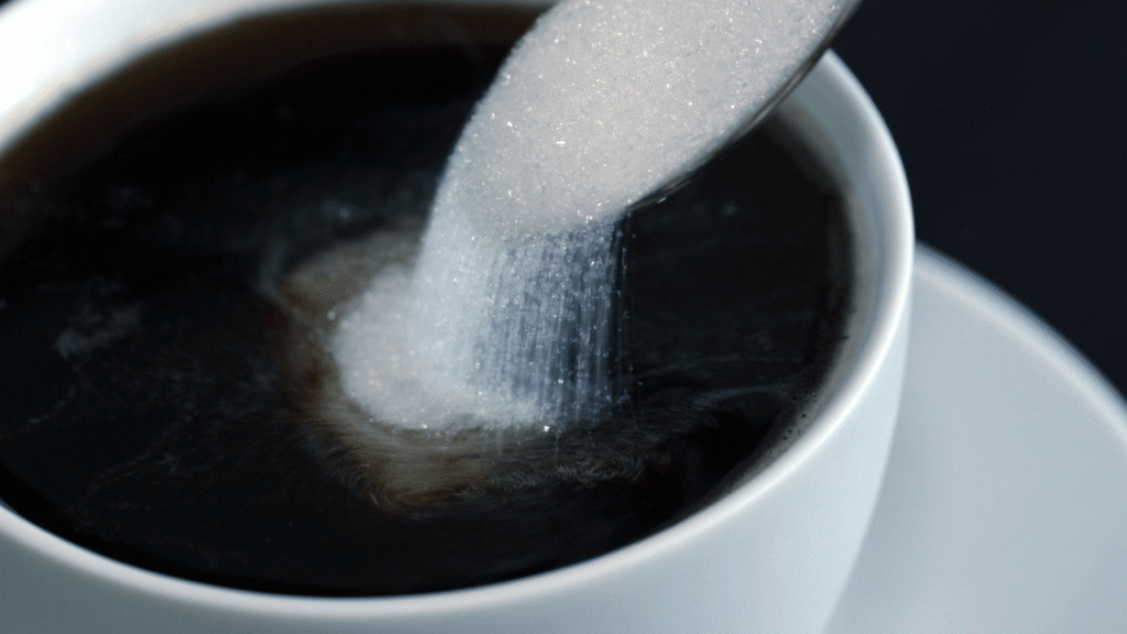 Reduce sugar intake with a mindful start—see how a spoonful of sugar pours into a cup of black coffee, highlighting the choice to cut back on sweeteners for a healthier daily habit.