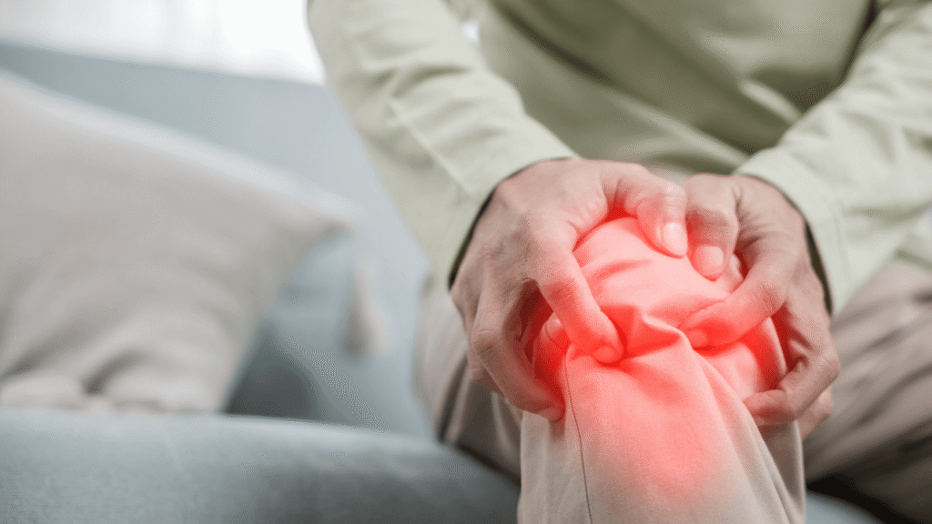 Exercises for joint health can start with understanding pain points like this image shows—a person gently holding a knee with a highlighted red area, signaling discomfort while sitting on a cozy couch. This visual emphasizes the need for gentle movement to ease joint stiffness.
